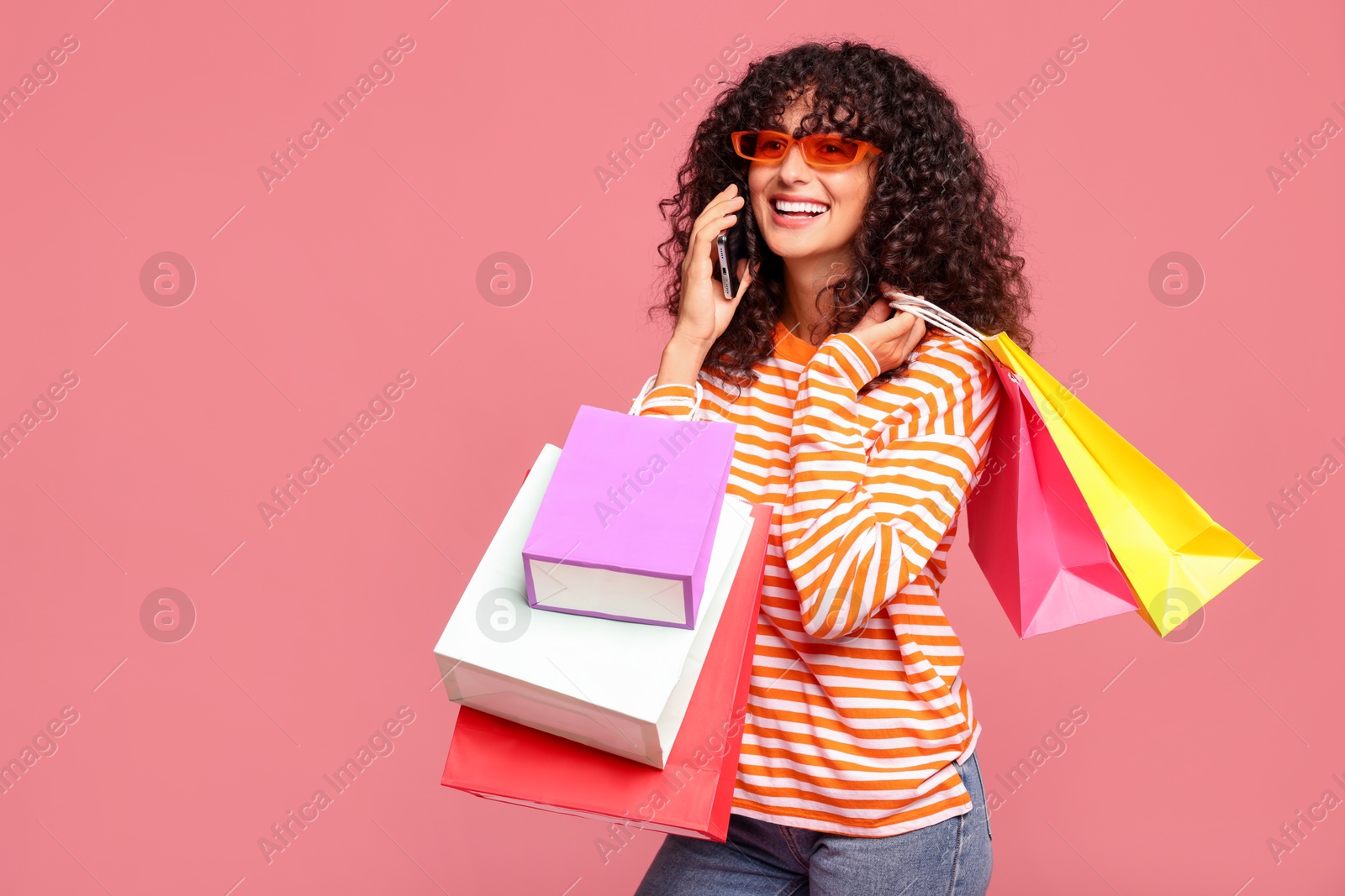 Photo of Smiling woman with colorful shopping bags talking by smartphone on pink background. Space for text