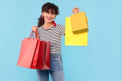 Photo of Smiling woman with colorful shopping bags on light blue background