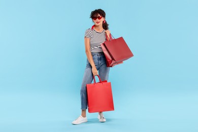 Beautiful woman with shopping bags on light blue background. Space for text