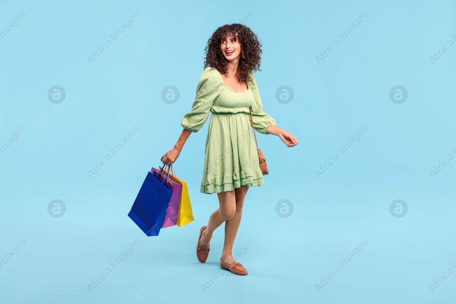 Photo of Smiling woman with colorful shopping bags on light blue background