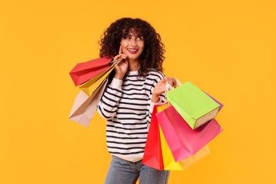 Smiling woman with colorful shopping bags on yellow background