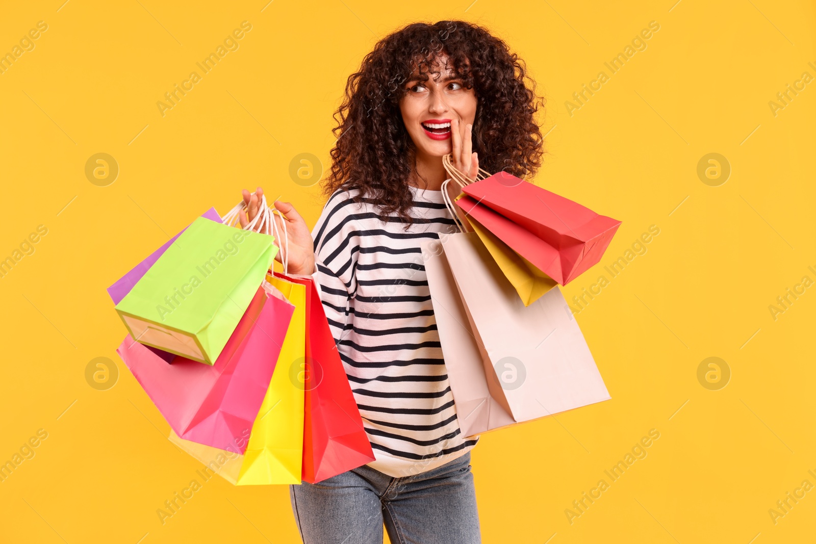 Photo of Happy woman with colorful shopping bags on yellow background