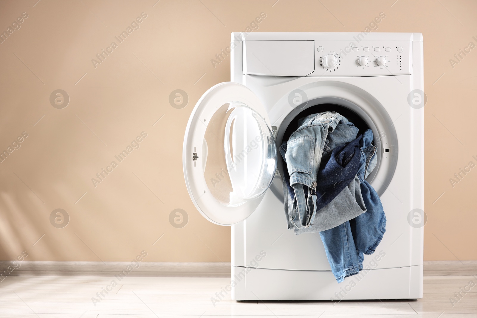 Photo of Washing machine with dirty jeans and other denim clothes indoors, space for text