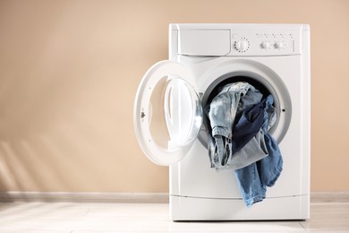 Photo of Washing machine with dirty jeans and other denim clothes indoors, space for text