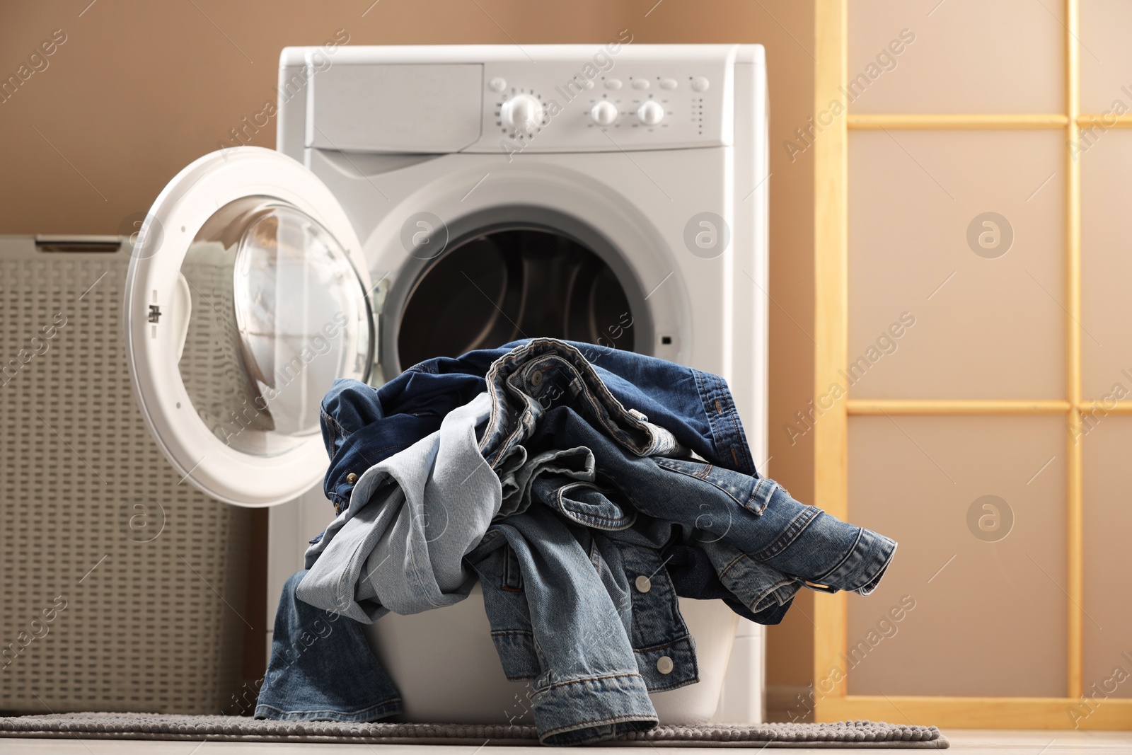 Photo of Washing machine with dirty jeans and other denim clothes indoors