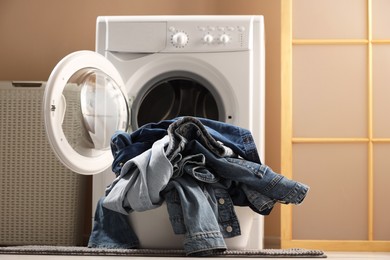 Photo of Washing machine with dirty jeans and other denim clothes indoors