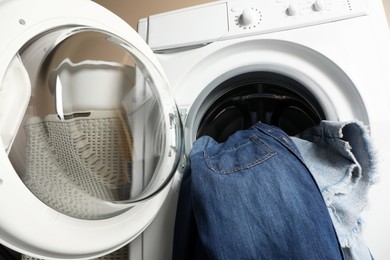 Photo of Washing machine with dirty jeans and other denim clothes indoors, closeup