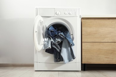 Photo of Washing machine with dirty jeans and other denim clothes indoors