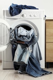 Photo of Washing machine with dirty jeans and other denim clothes indoors