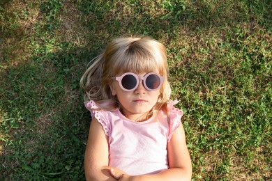 Photo of Cute little girl resting on green lawn in park, top view