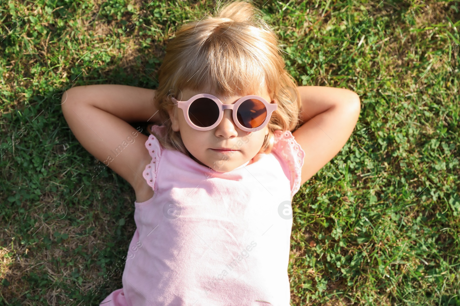 Photo of Cute little girl resting on green lawn in park, top view