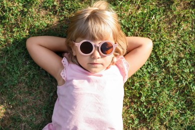 Cute little girl resting on green lawn in park, top view