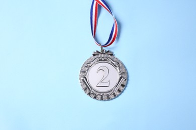 Photo of One silver medal on light blue background, top view