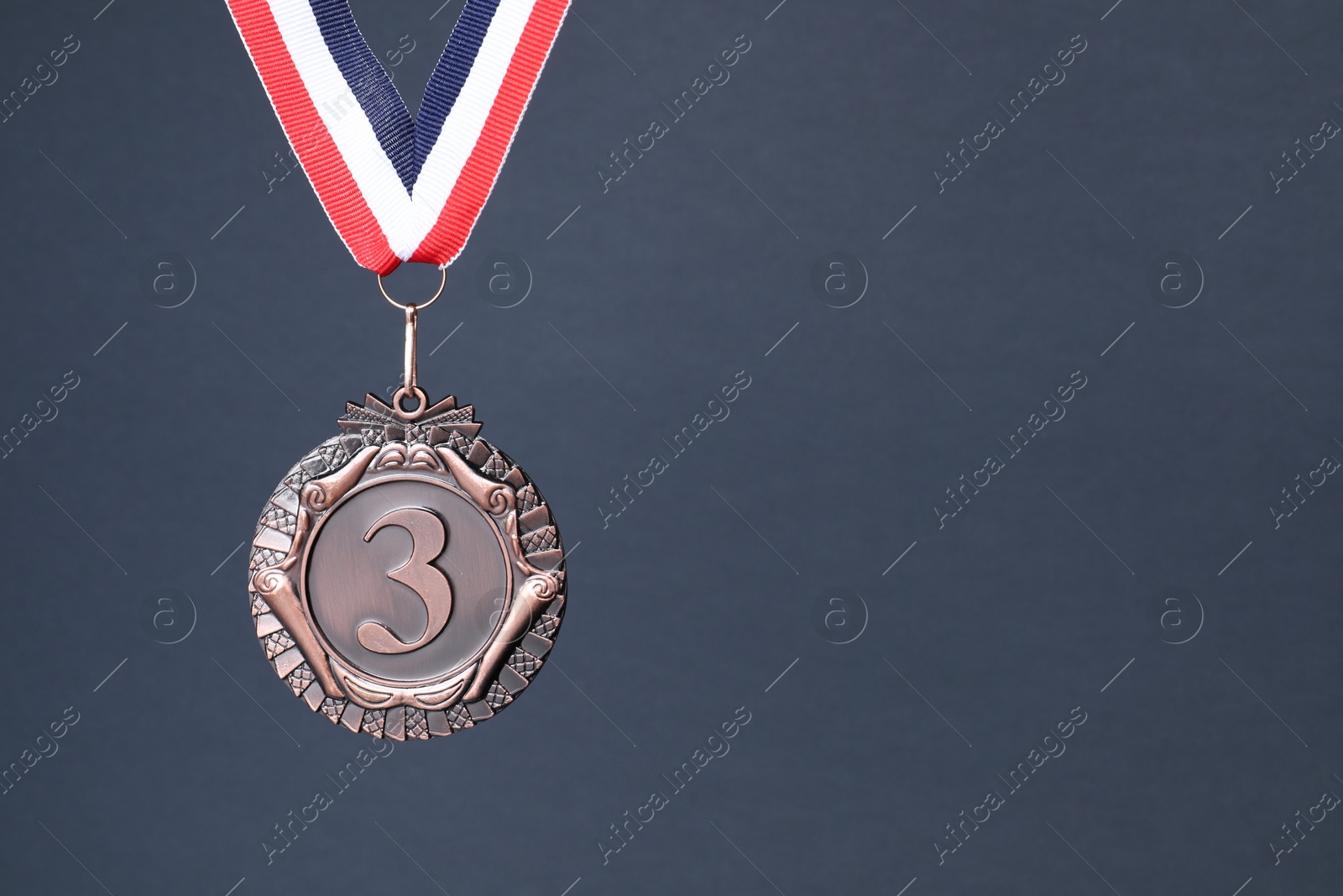 Photo of Bronze medal with striped ribbon on grey background, space for text