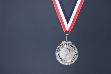 Photo of Silver medal with striped ribbon on grey background, space for text