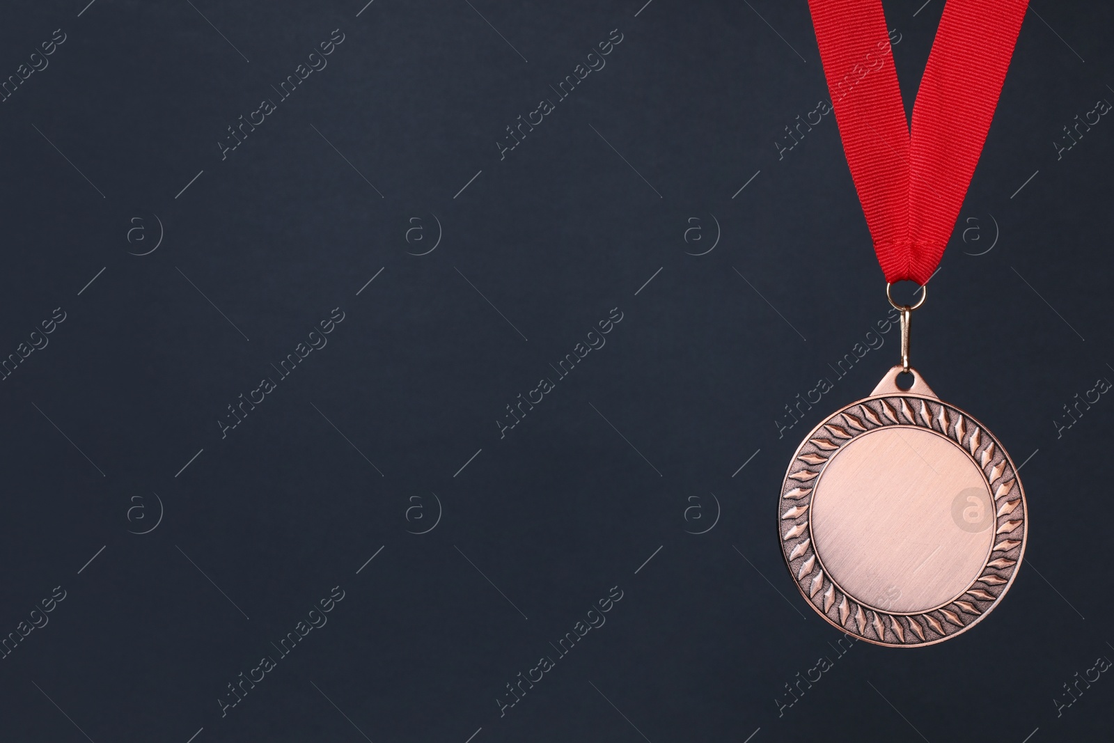 Photo of Bronze medal with red ribbon on dark grey background, space for text