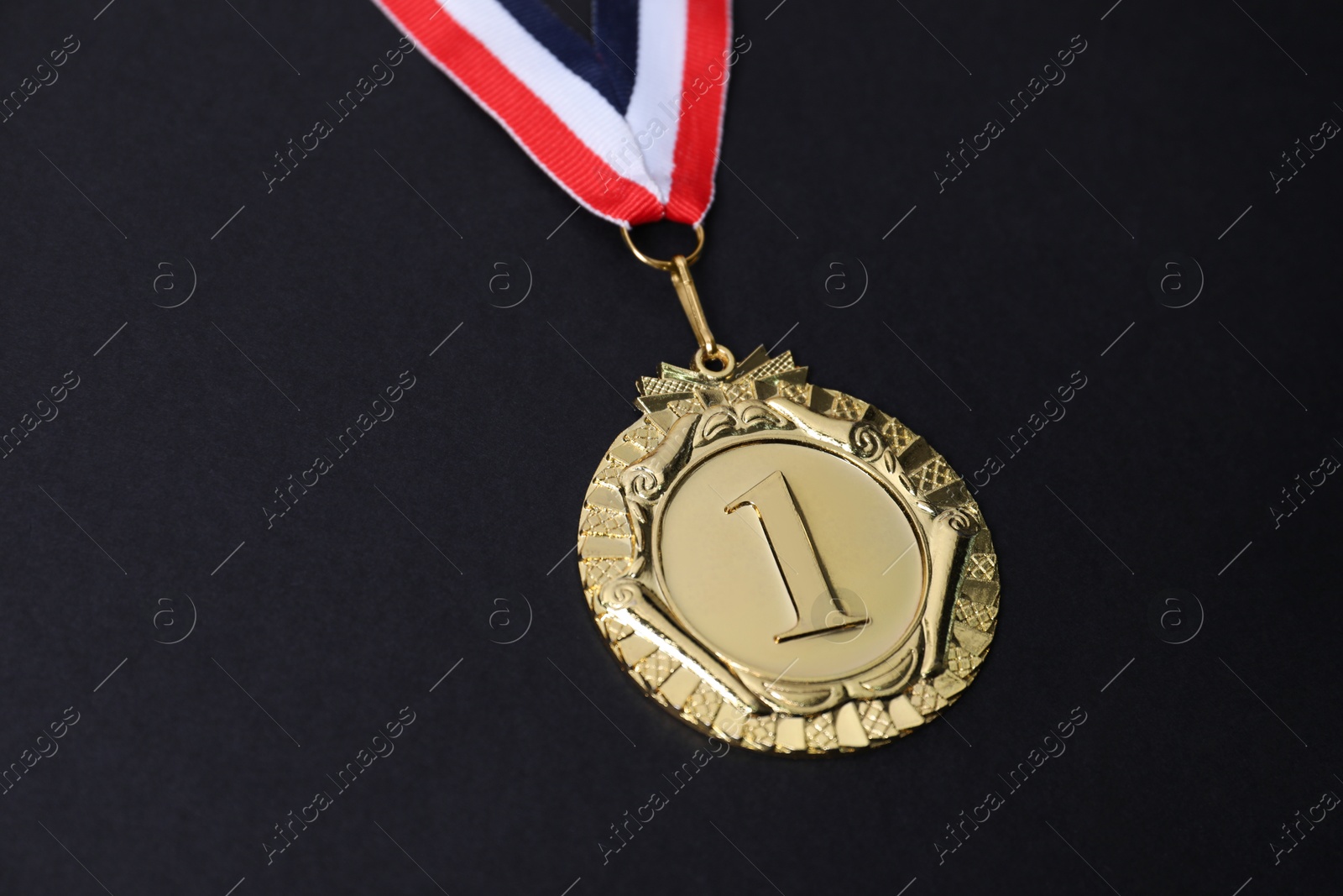 Photo of Golden medal with striped ribbon on black background, closeup