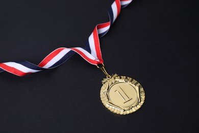 Photo of Golden medal with striped ribbon on black background, closeup