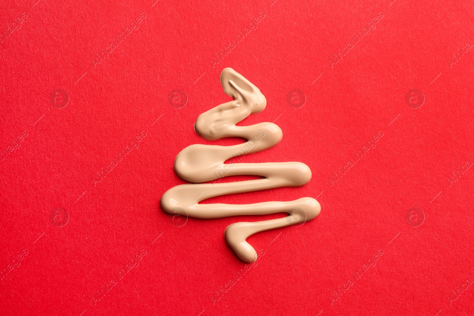 Photo of Christmas tree made of skin foundation on red background, top view