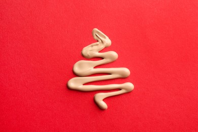 Christmas tree made of skin foundation on red background, top view