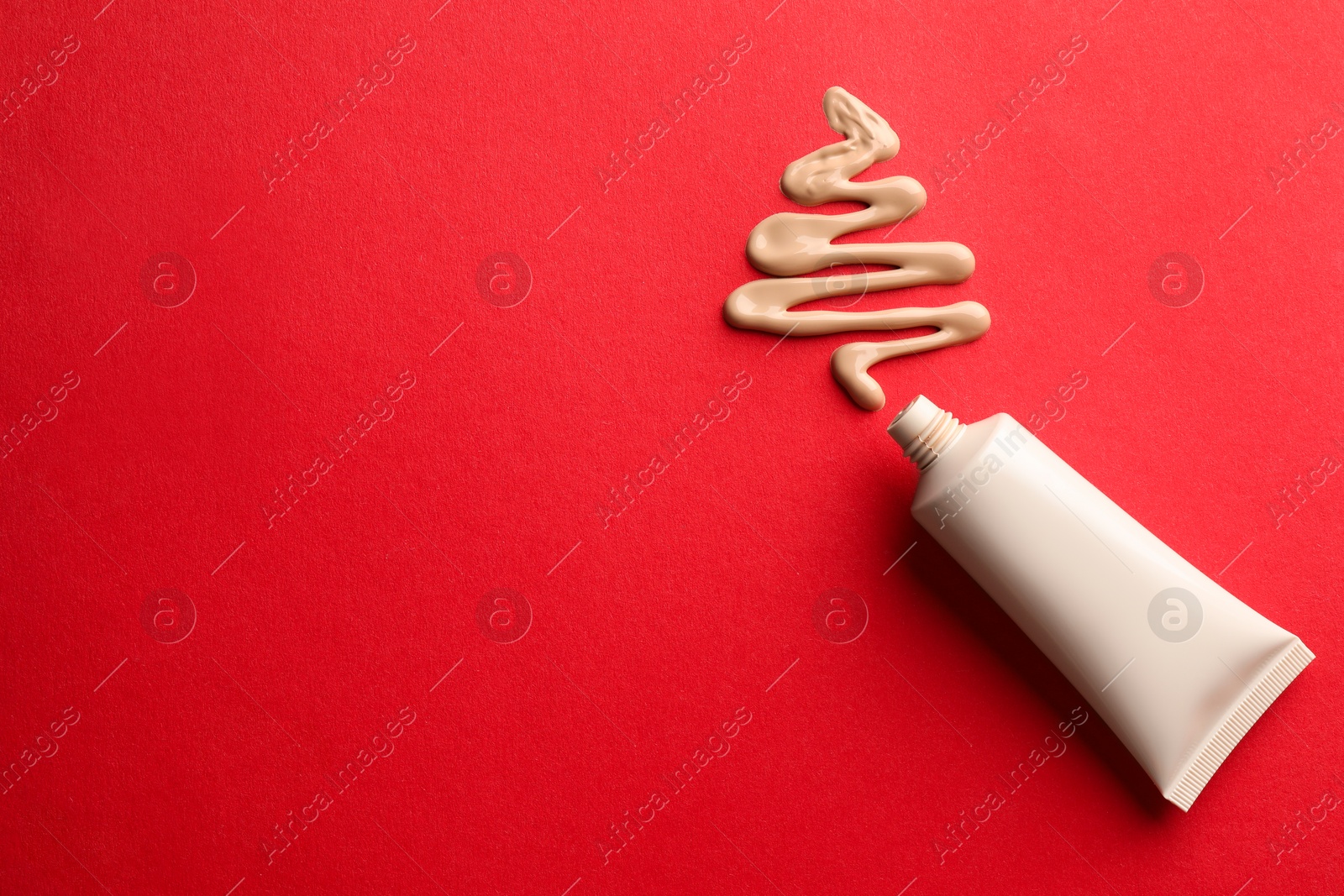 Photo of Christmas tree made of skin foundation and tube on red background, top view. Space for text