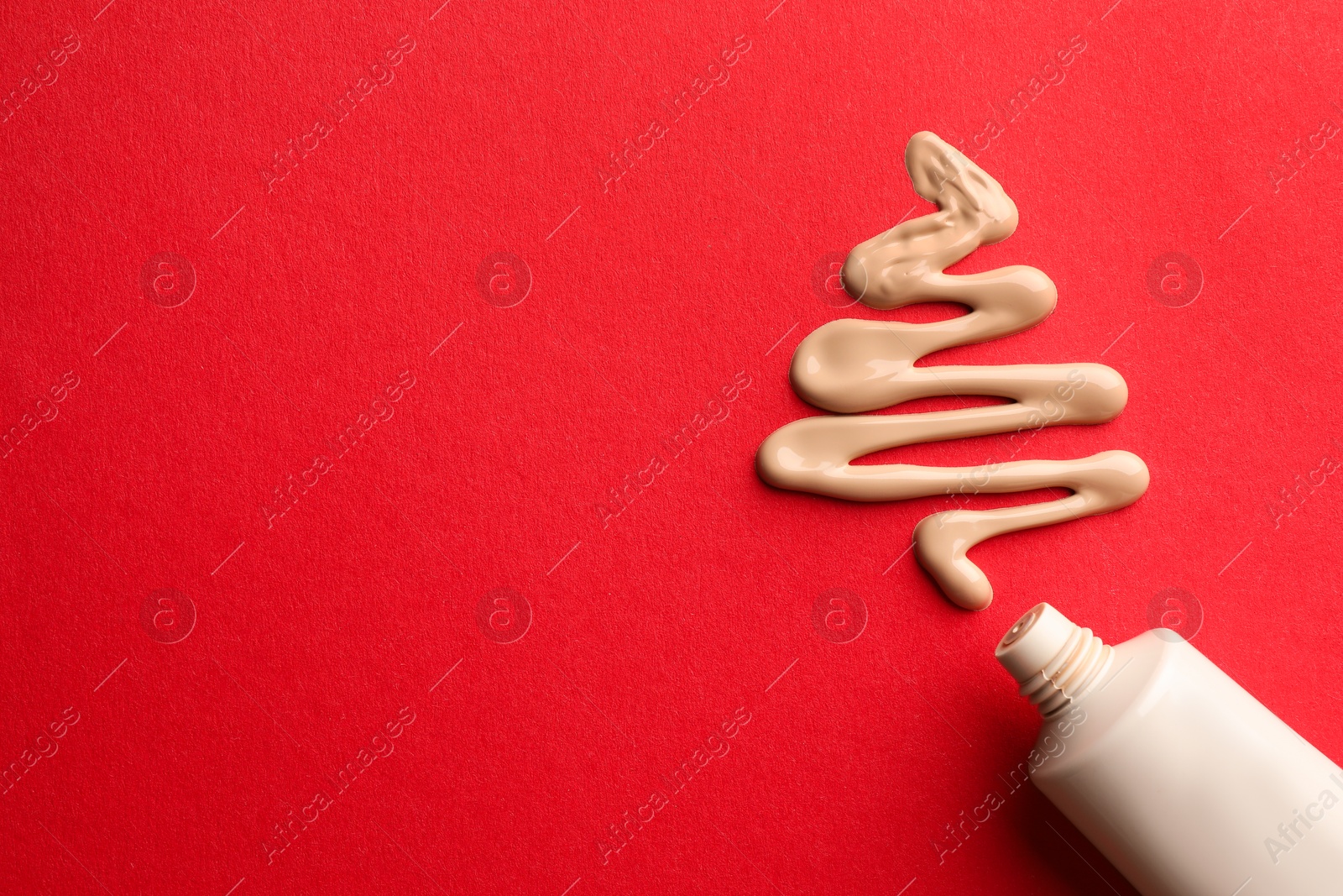 Photo of Christmas tree made of skin foundation and tube on red background, top view. Space for text