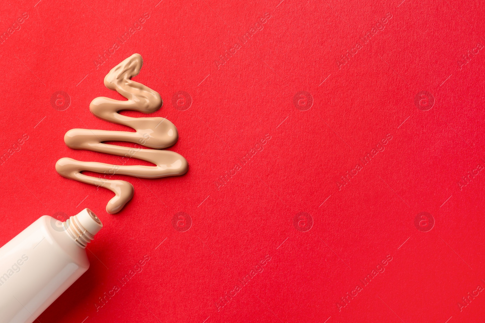 Photo of Christmas tree made of skin foundation and tube on red background, top view. Space for text