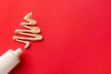 Christmas tree made of skin foundation and tube on red background, top view. Space for text