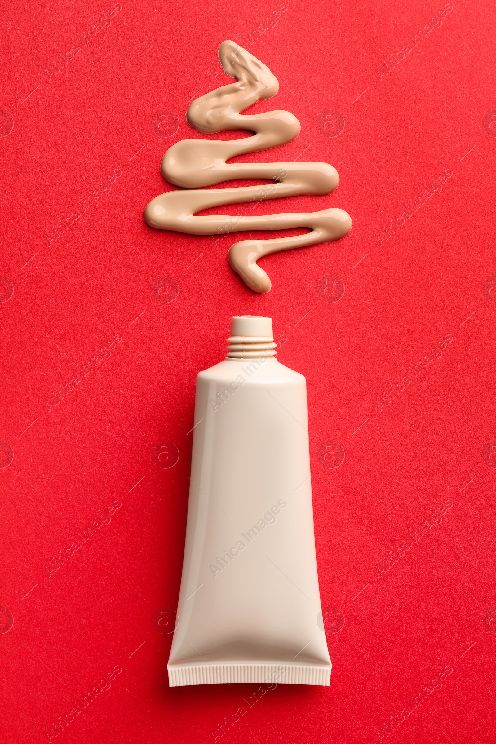 Photo of Christmas tree made of skin foundation and tube on red background, top view