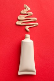 Christmas tree made of skin foundation and tube on red background, top view