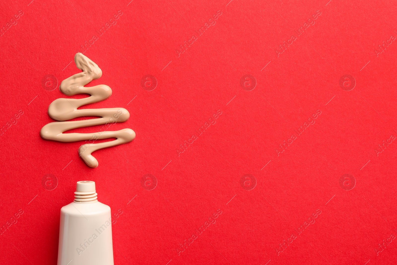 Photo of Christmas tree made of skin foundation and tube on red background, top view. Space for text