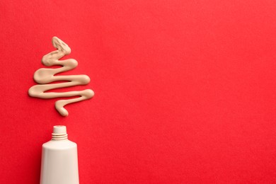 Photo of Christmas tree made of skin foundation and tube on red background, top view. Space for text