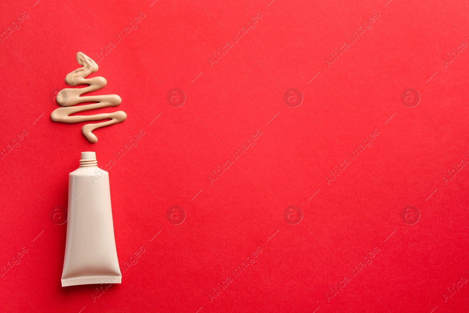 Photo of Christmas tree made of skin foundation and tube on red background, top view. Space for text