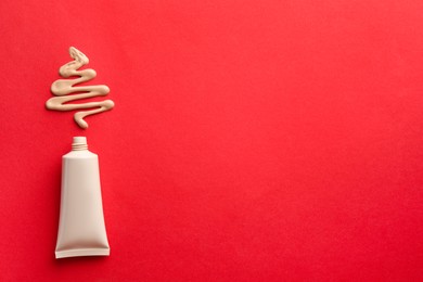 Photo of Christmas tree made of skin foundation and tube on red background, top view. Space for text