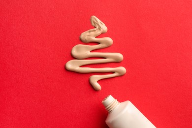 Photo of Christmas tree made of skin foundation and tube on red background, top view