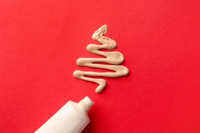 Christmas tree made of skin foundation and tube on red background, top view