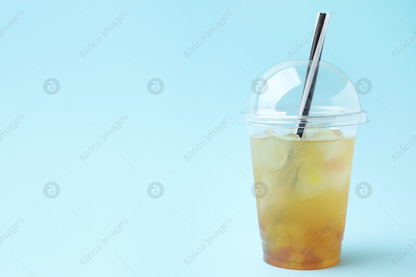 Photo of Tasty bubble tea in plastic cup on light blue background, space for text