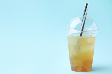 Photo of Tasty bubble tea in plastic cup on light blue background, space for text