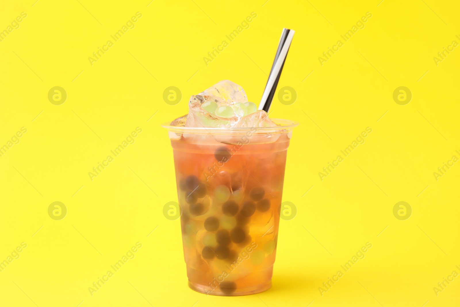 Photo of Tasty bubble tea in plastic cup on yellow background