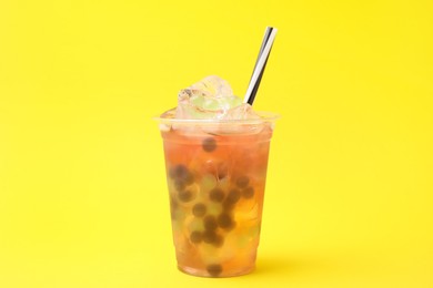 Photo of Tasty bubble tea in plastic cup on yellow background