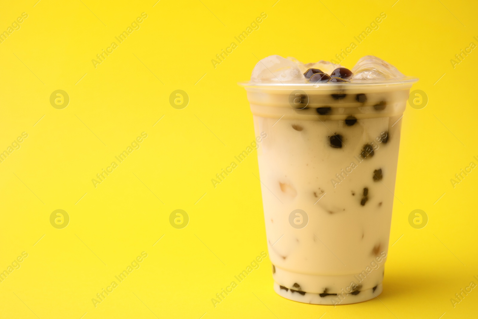 Photo of Tasty milk bubble tea in plastic cup on yellow background, space for text