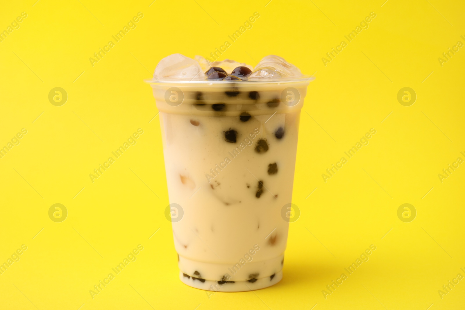 Photo of Tasty milk bubble tea in plastic cup on yellow background