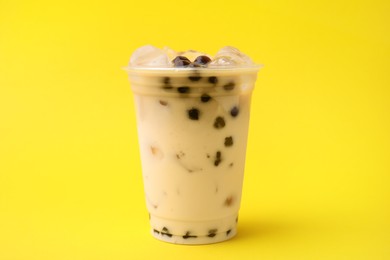 Photo of Tasty milk bubble tea in plastic cup on yellow background