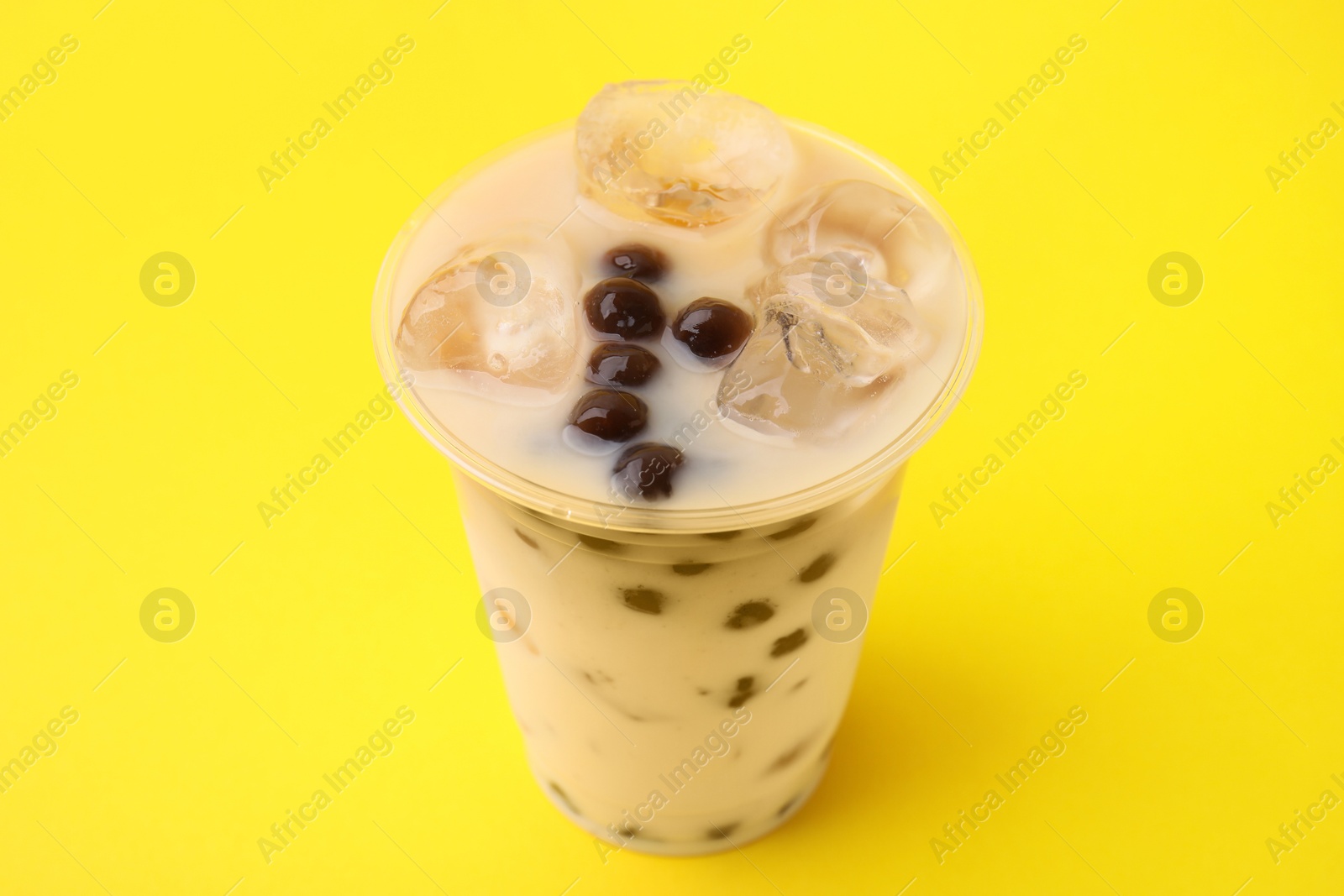 Photo of Tasty milk bubble tea in plastic cup on yellow background, closeup