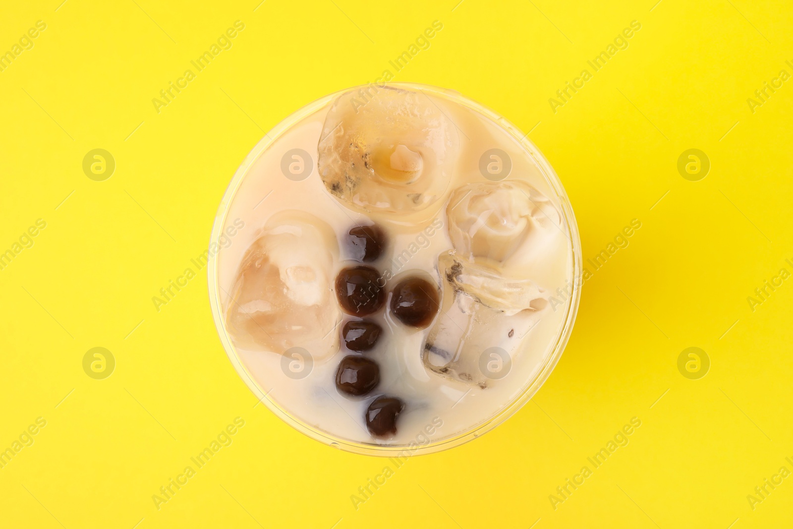 Photo of Tasty milk bubble tea in plastic cup on yellow background, top view