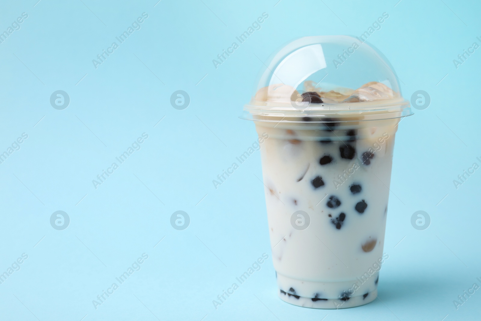 Photo of Tasty milk bubble tea in plastic cup on light blue background, space for text