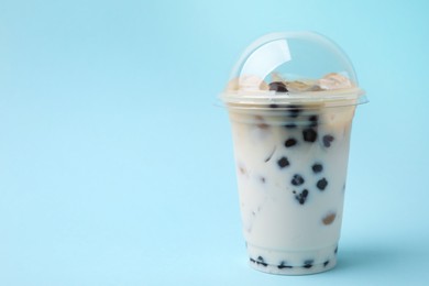 Tasty milk bubble tea in plastic cup on light blue background, space for text