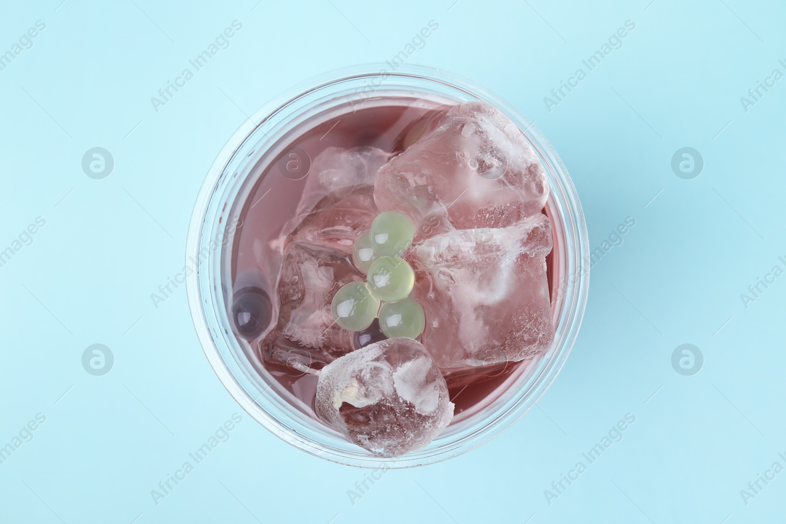 Photo of Tasty bubble tea in plastic cup on light blue background, top view