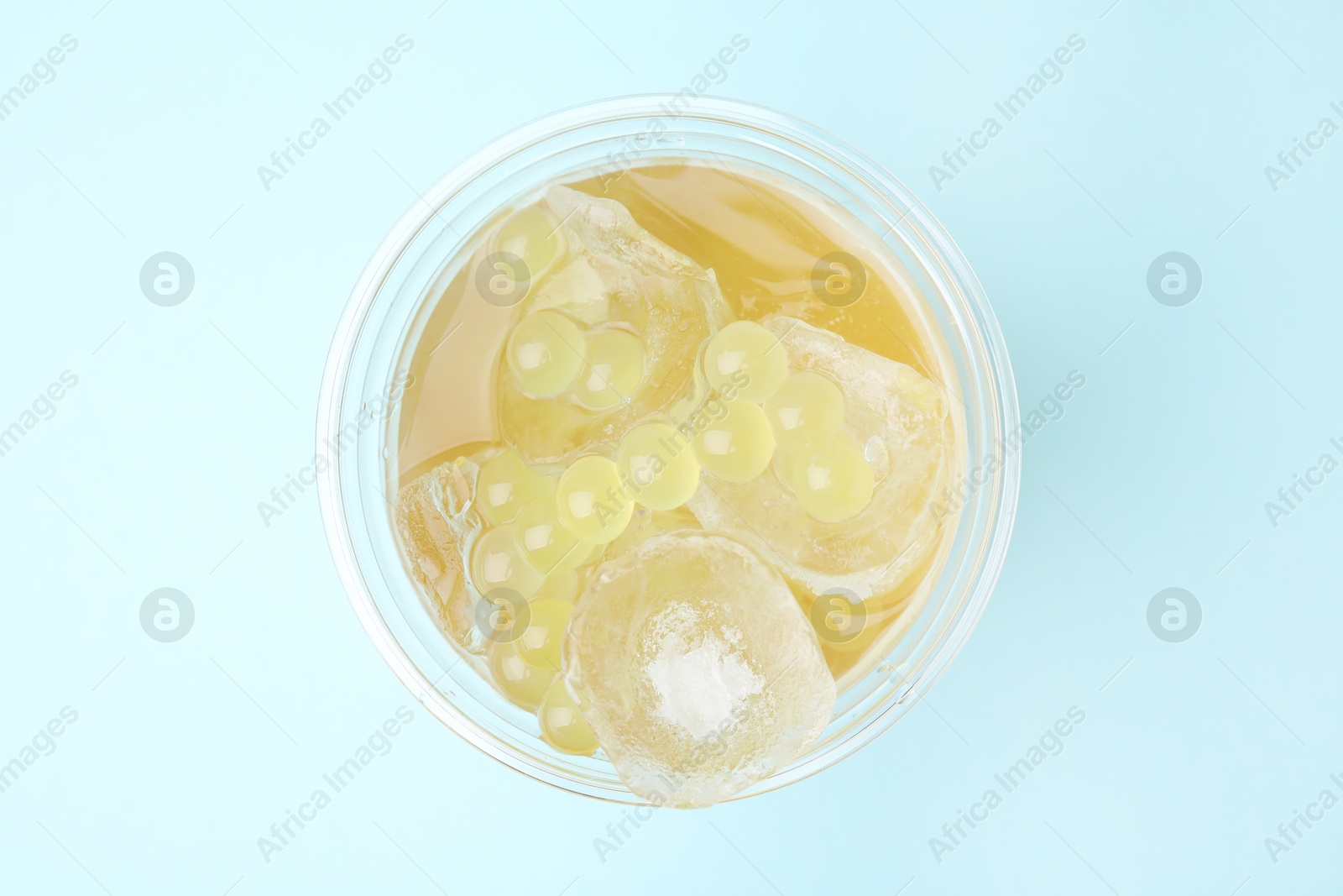 Photo of Tasty bubble tea in plastic cup on light blue background, top view