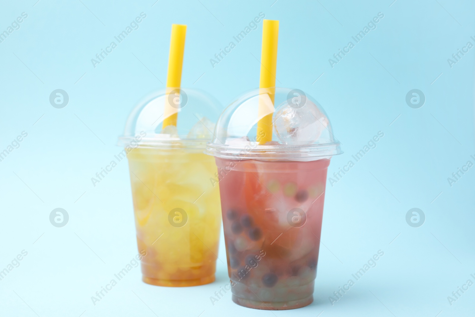 Photo of Tasty bubble tea in plastic cups on light blue background